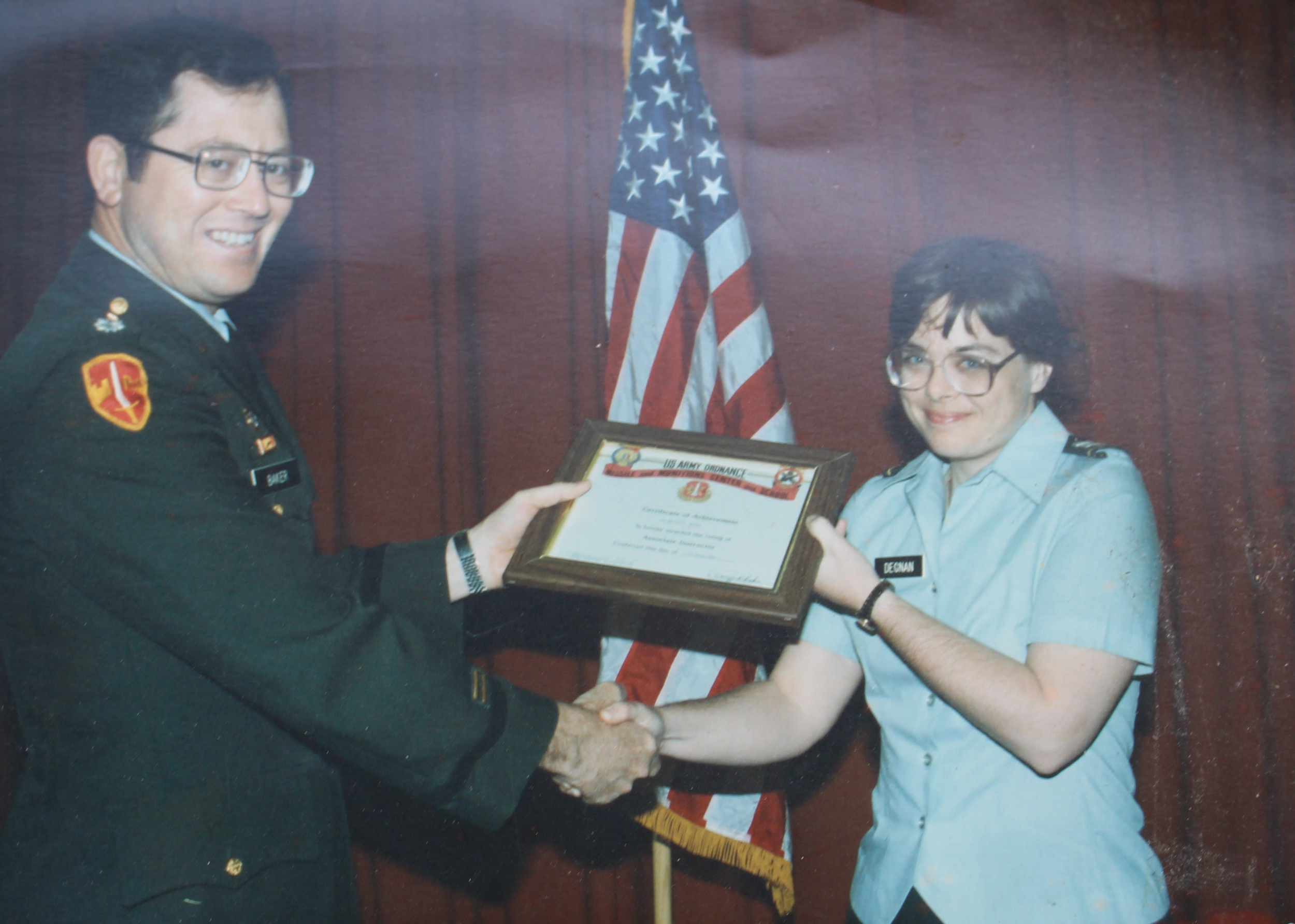 A woman shakes hands and accepts a framed certificate from a man dressed in Army uniform.