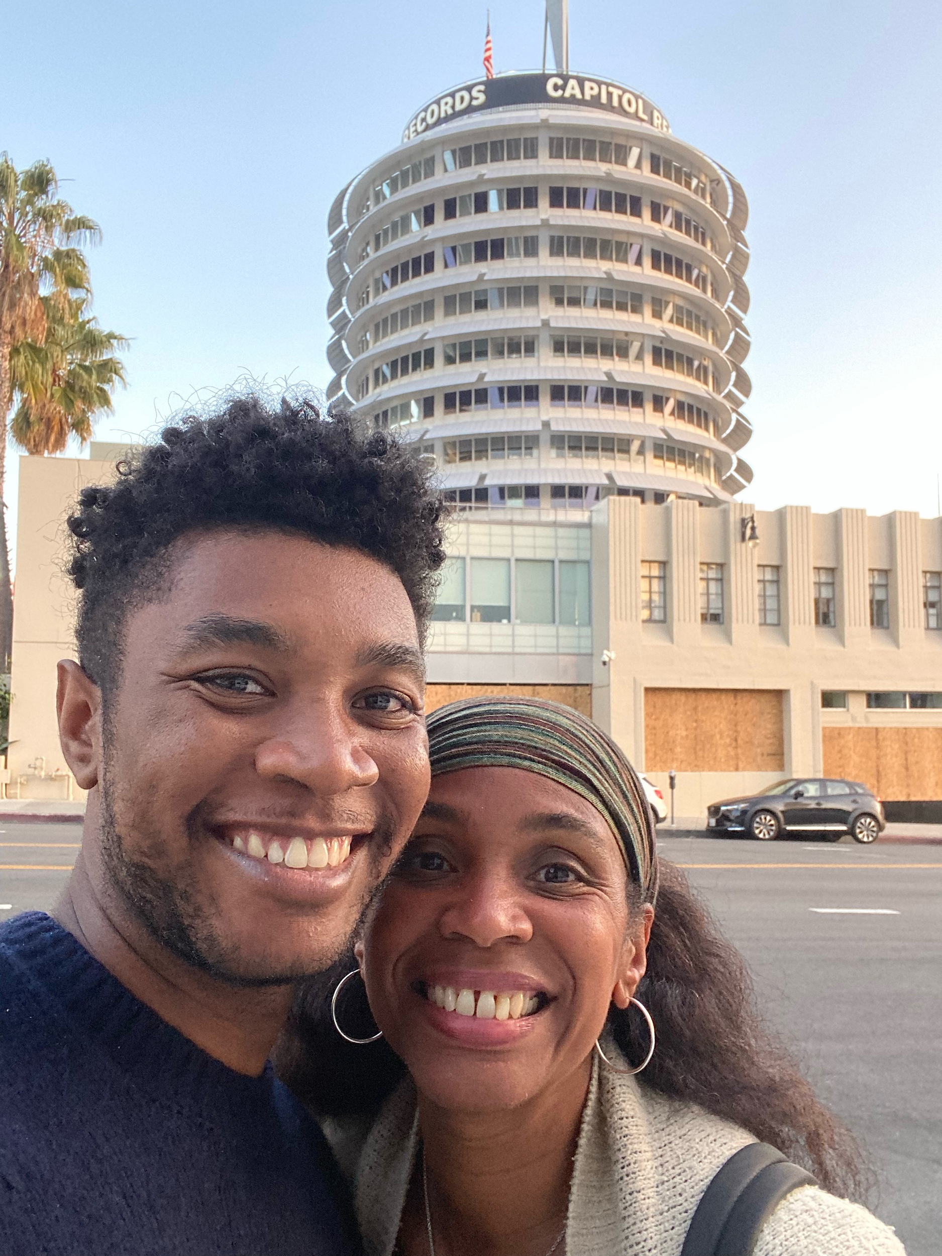 A selfie of a young man and his mother smiling and in an embrace, standing in front of the Capitol Records building in Hollywood.